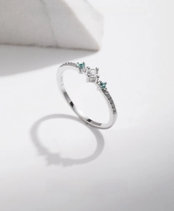 Close-up of S925 silver ring with white zircon and two green gemstones on marble