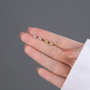 Mini S999 sterling silver bow stud earrings in gold and silver finish on fingertips