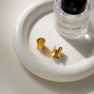 Minimalist gold-plated C-shaped ear cuffs with micro-beaded edges on a ceramic dish