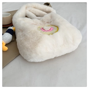Detail of white plush shoulder bag with donut embroidery on a cozy textile surface