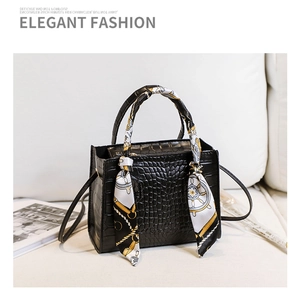 Détail d'un sac à main noir à motif crocodile avec foulard décoratif sur la poignée