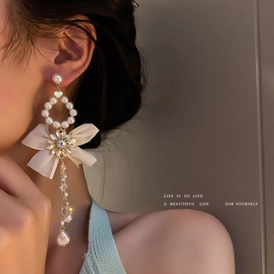 Elegant asymmetric bow tassel earrings with faux pearls and rhinestones on female model