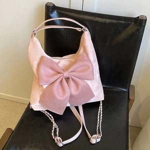 Pink velvet handbag with large bow and metal chain strap shown on dark chair