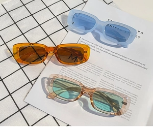 Three pairs of vintage square sunglasses in blue, amber, and pink on a textured background
