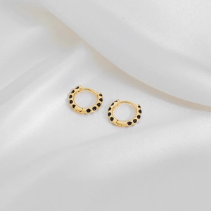 Detailed close-up of gold hoop earrings with black polka dots on white silk fabric