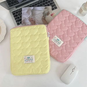Detailed view of heart-quilted yellow and pink iPad laptop sleeves on a minimalist desk