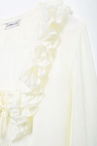 Detailed view of white V-neck chiffon shirt with ruffle edges and lace-up bow