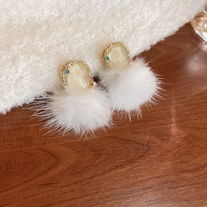Detail of elegant gold earrings featuring white rhinestones and soft plush fur balls