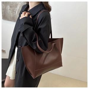 Grand sac cabas minimaliste en cuir marron porté avec un trench noir pour un look urbain