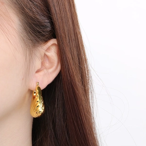 Detail of gold water-drop earring with leaf texture worn on a model's ear