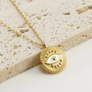 Minimalist gold stainless steel evil eye necklace with white enamel pendant on beige stone