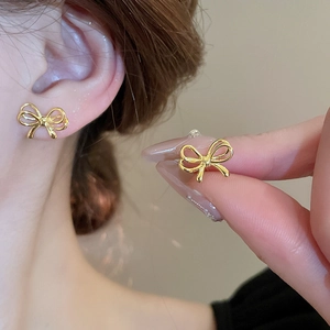 Elegant minimalist golden bow earrings for women shown on a model in a warm indoor setting