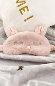 Detailed close-up of a soft pink plush rabbit sleep mask on a cozy striped blanket