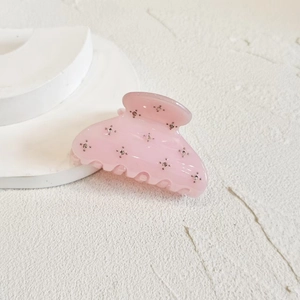 Detailed close-up of a pink rhinestone claw clip on a clean geometric background