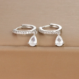 Macro shot of silver teardrop earrings with sparkling cubic zirconia on brown leather