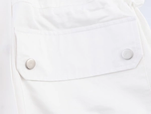 Detailed macro view of a white cotton utility jacket pocket with silver metal snap buttons