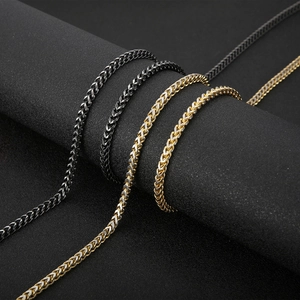 Macro shot of titanium steel wheat chain necklaces in black, gold, and silver tones