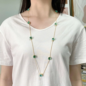 Detail of long gold chain necklace with square green crystal pendants on a white shirt
