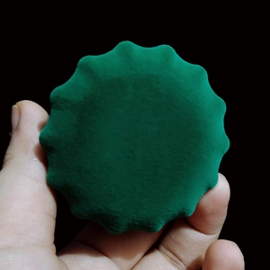 Detailed view of a green velvet round wave-edged jewelry box component on dark background