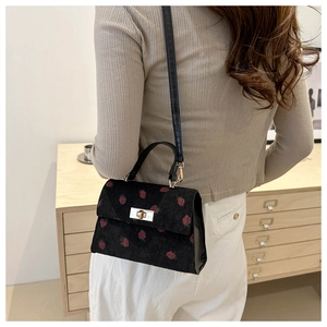 Detail of black corduroy mini bag featuring strawberry print and gold metal twist lock