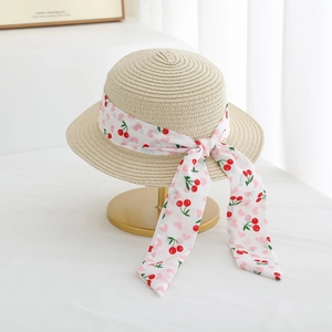 Close-up of children's straw hat with cherry print ribbon bow on a golden display stand