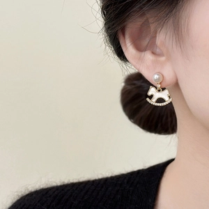 Detail of a gold plated rocking horse earring with pearls and rhinestones on a model
