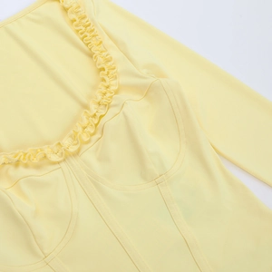 Detail view of pale yellow long sleeve top with ruffle neckline and structured seams