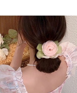 Close-up of a large pink fabric rose hair scrunchie with green leaves on a woven basket