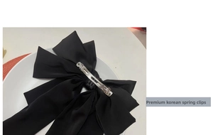 Detail of a large black satin bow hair clip featuring a durable silver metal spring clasp