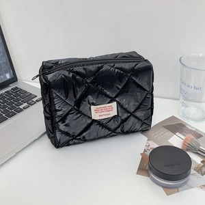 Detail of a black quilted makeup bag with zipper closure on a white desk setup