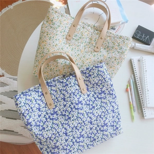 Flat lay of small floral canvas tote bags with leather handles on a white table