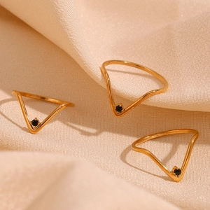 Three gold V-shaped rings featuring micro-set black stones on soft peach fabric background