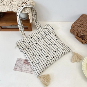 Dettaglio della borsa tote in tela a cuore con nappe decorative su sfondo vintage curato