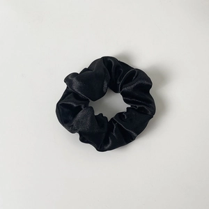 Detailed close-up of a black satin scrunchie with soft pleated silk texture and elastic core