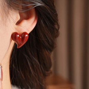 Macro side view of a glossy red heart stud earring worn on ear with soft warm background