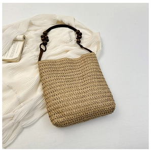 Detail of bohemian straw handbag with dark wood bead handles on a soft white background