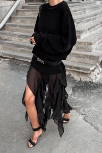 Detail of chunky black knit sweater paired with a tiered ruffled high-slit chiffon skirt