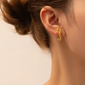 Detailed close-up of golden seahorse-shaped stud earrings with zircon inlay on model