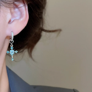 Close-up of diamond cross pendant earring with blue and white stones on earlobe