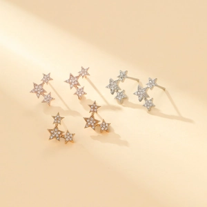 Close-up of star-shaped stud earrings in rose gold, gold, and silver with zircon stones