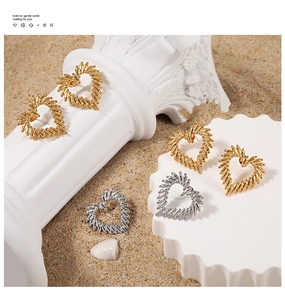 Close-up of gold and silver textured hollow heart earrings on white pedestal