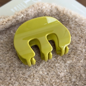 Detailed view of glossy green M-shaped acrylic hair claw clip on soft beige fabric