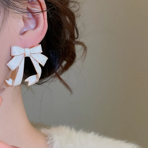 Macro shot of an elegant white enamel bow earring with gold trim worn by a model