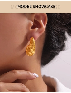 Detail of gold U-shaped oval earrings with grainy textured finish on female model