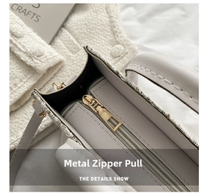 Close-up of golden metal zipper on white leather and tweed plaid small square bag