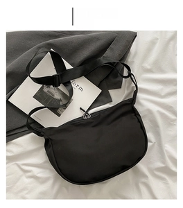 Detail view of a black crescent nylon crossbody bag on white linen with a wide strap