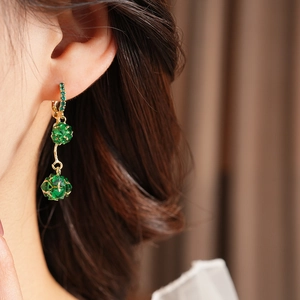 Close-up of vintage gold drop earrings with faceted green crystals worn by a model