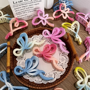 Gradient bow hair claw clips in matte resin displayed on an elegant woven tray