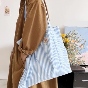 Borsa tote in tela a righe blu e bianche con etichetta Bébé, vista laterale su modella