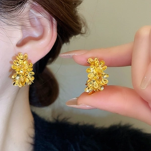 Detail showing the 3D gold floral cluster earrings worn on ear and held in hand